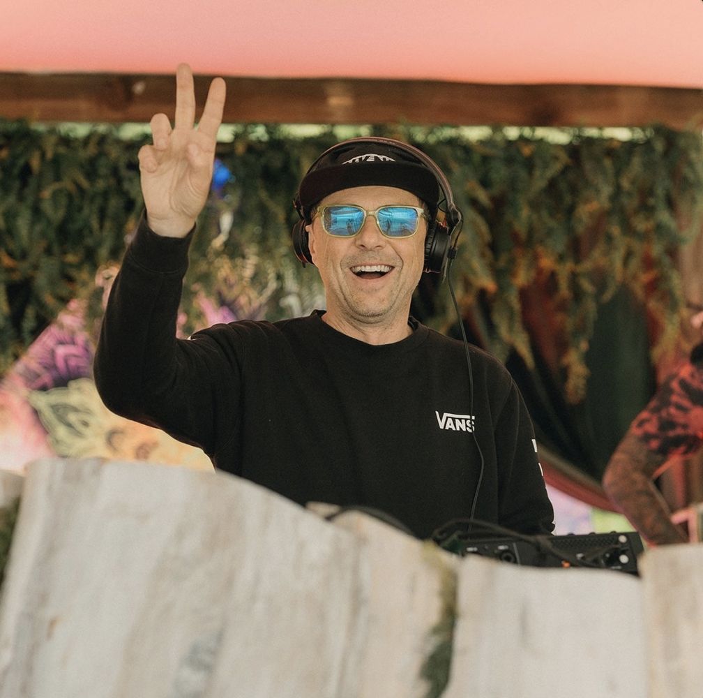 Late Nite Guest smiling behind the decks with a peace sign at an outdoor festival stage