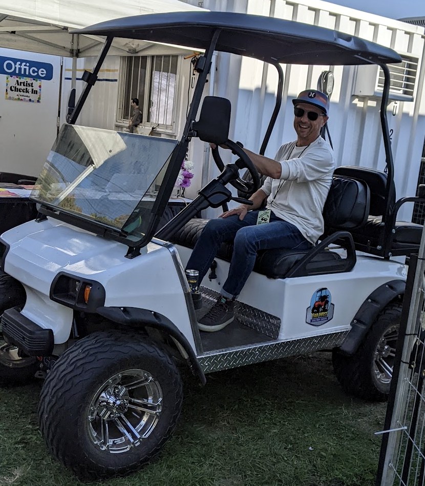 Sean driving a festival golf cart backstage, outside the production office and artist check-in